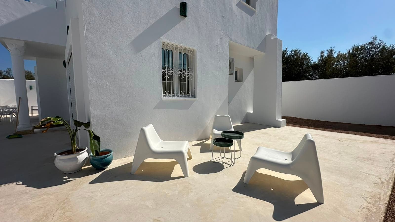 Le patio en plein soleil, deux fauteuils blancs devant la maison