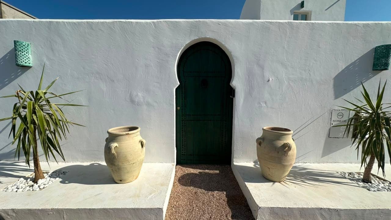 La porte verte en arc de Casa Noah, entre deux jarres