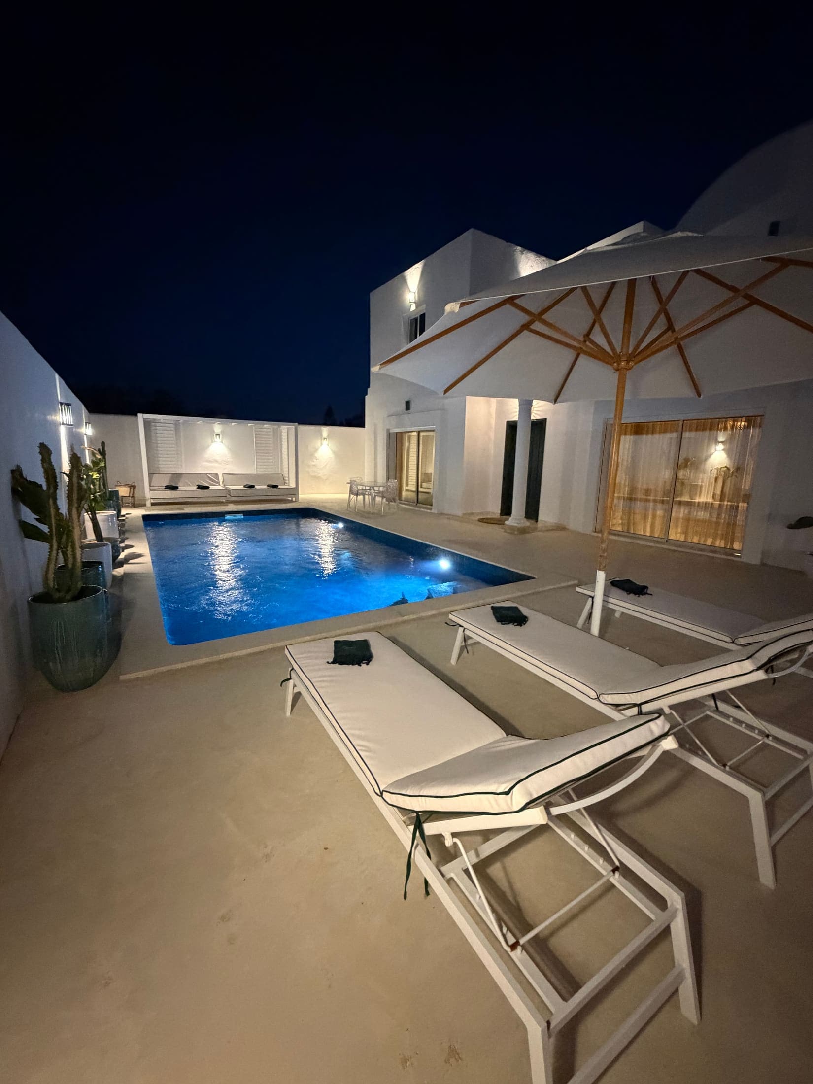 Les transats au bord de la piscine éclairée, la maison illuminée derrière