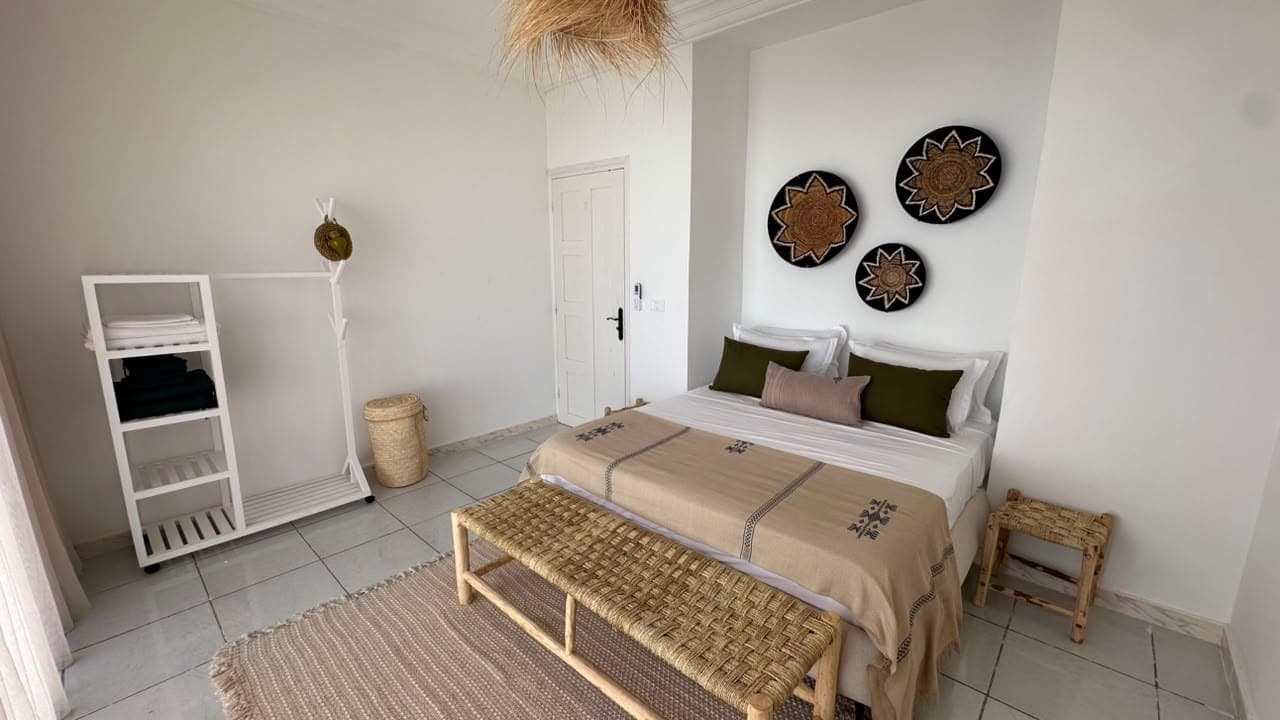 La chambre, lit double, banc tressé et paniers au mur